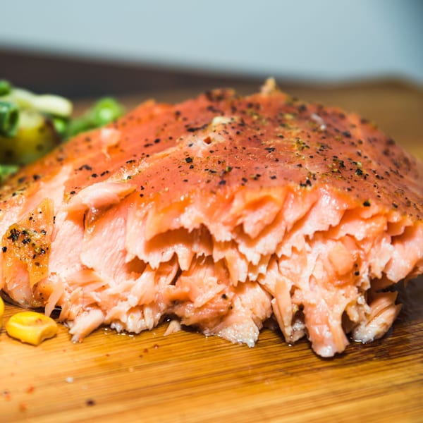 Close-up of a perfectly cooked, flaky salmon fillet seasoned with black pepper on a wooden board.