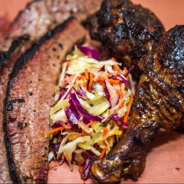 The Taste Smokers' BBQ platter with sliced brisket, dark chicken, and colorful coleslaw.