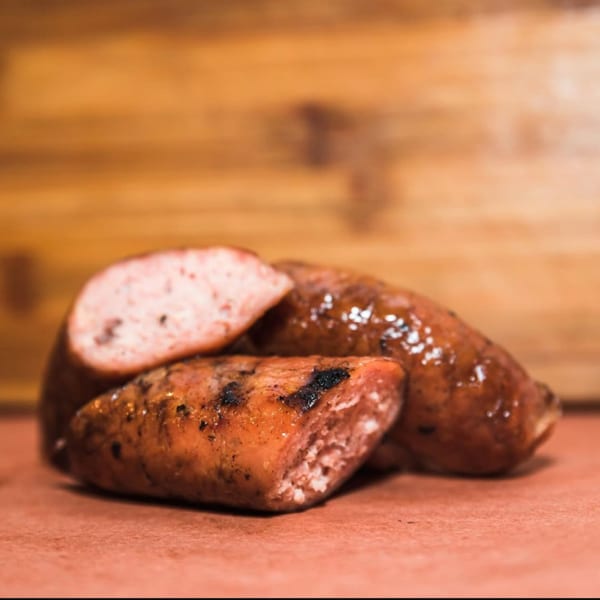 Three grilled sausages, one sliced open, on a reddish-brown surface with a wooden background.