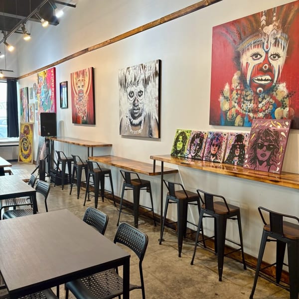 The Taste Smokers restaurant interior with vibrant art, high-top tables, and bar stools along a wall.