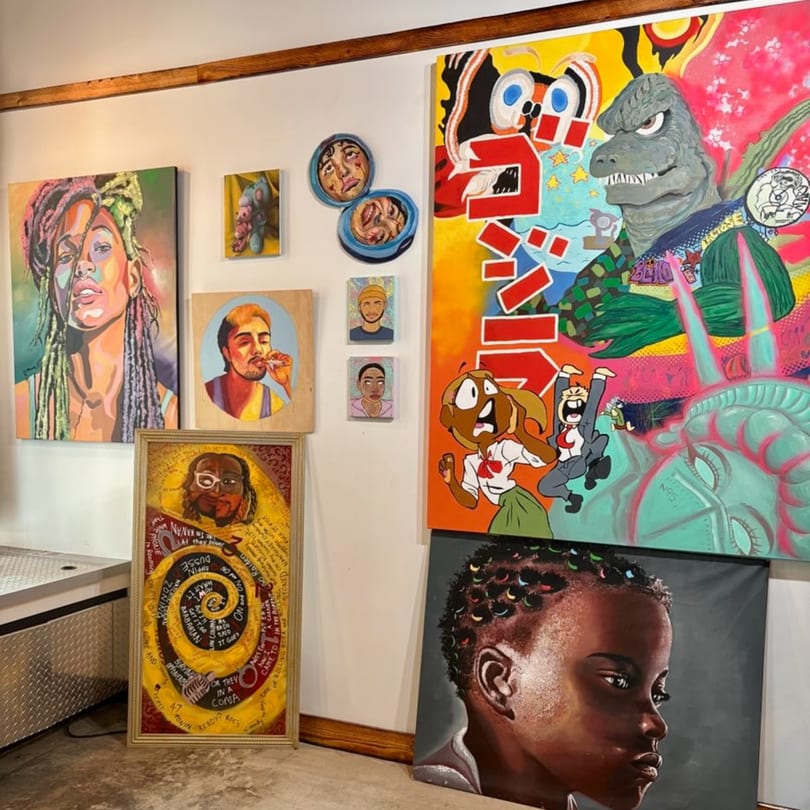A wall covered with vibrant, diverse paintings, including portraits, abstract art, and pop culture references.